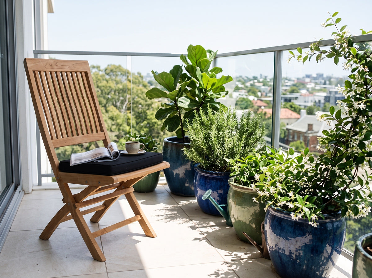 Teak Capri folding chair with black cushion on a sunny apartment balcony with potted plants