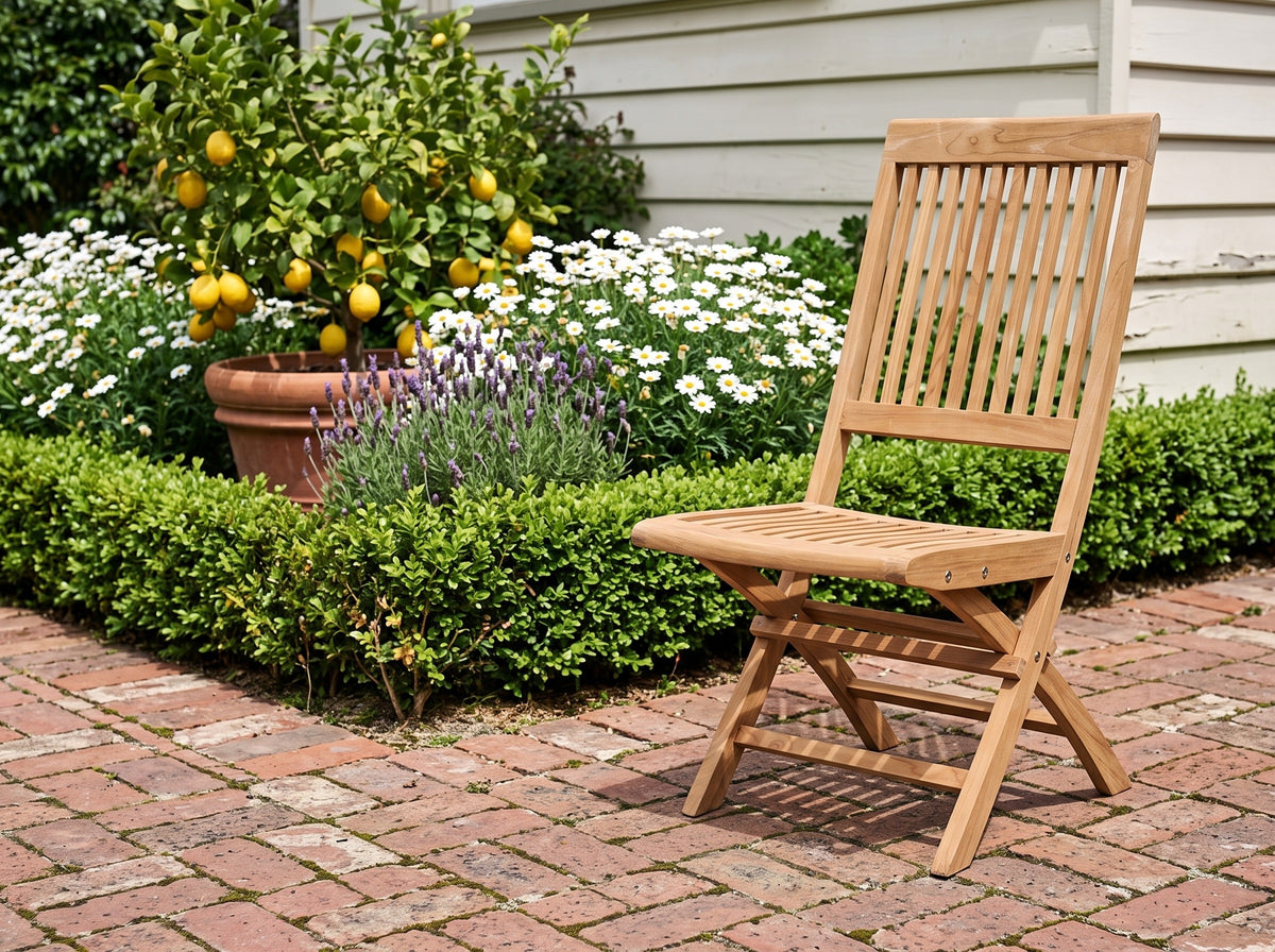 Teak Capri folding chair on red brick paving beside a potted lemon tree and white daisies
