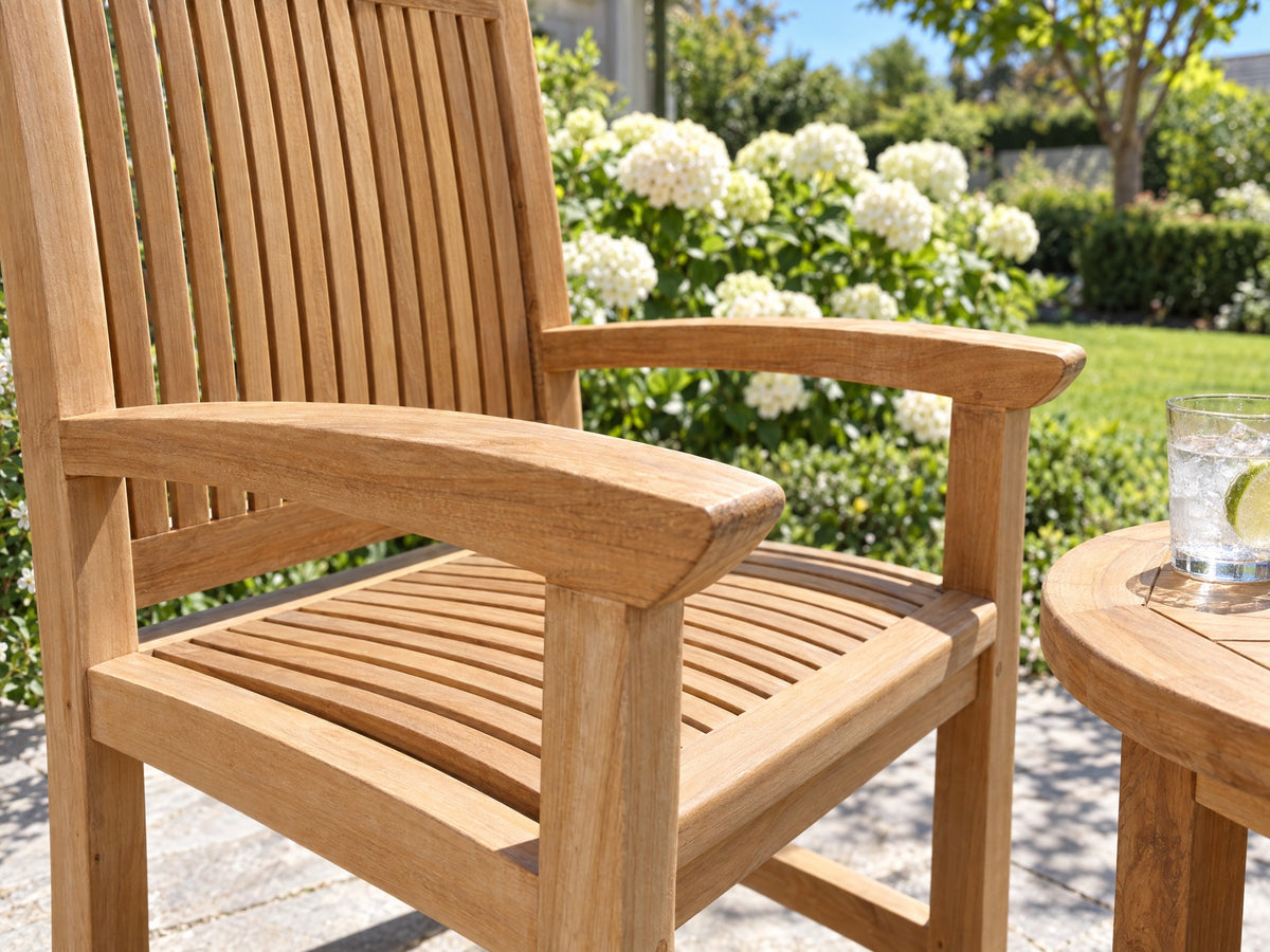 Close-up of the wide armrest of a teak Japan armchair beside a round teak side table, white hydrangeas behind