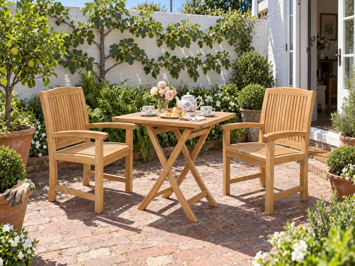 Two teak Japan armchairs at a square teak folding table in a brick-paved cottage courtyard