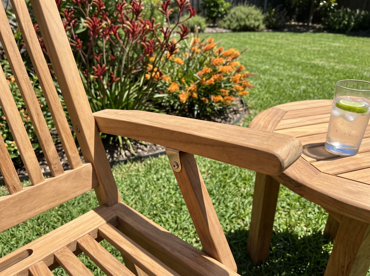 Close-up of the armrest of a teak Leo folding armchair beside a round teak side table, kangaroo paw behind