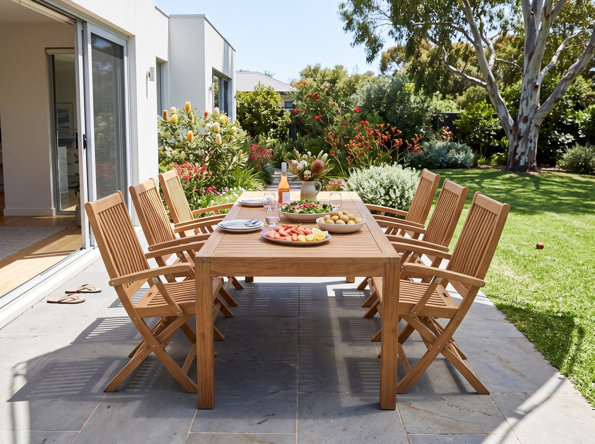 Teak Leo folding armchairs around a teak Deluxe dining table on a bluestone terrace beside a native garden