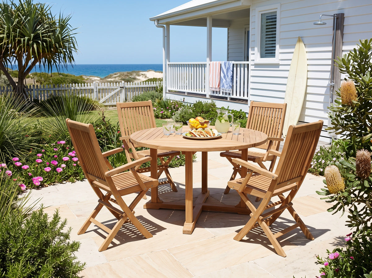 Teak Leo folding armchairs around a round teak Tye table in a coastal garden