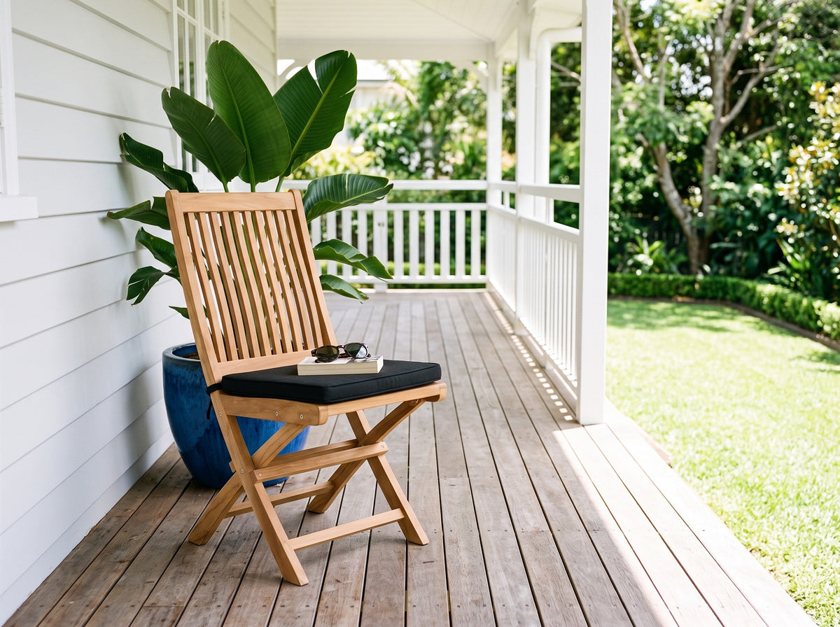 Teak Leo folding dining chair with black cushion on a white weatherboard verandah