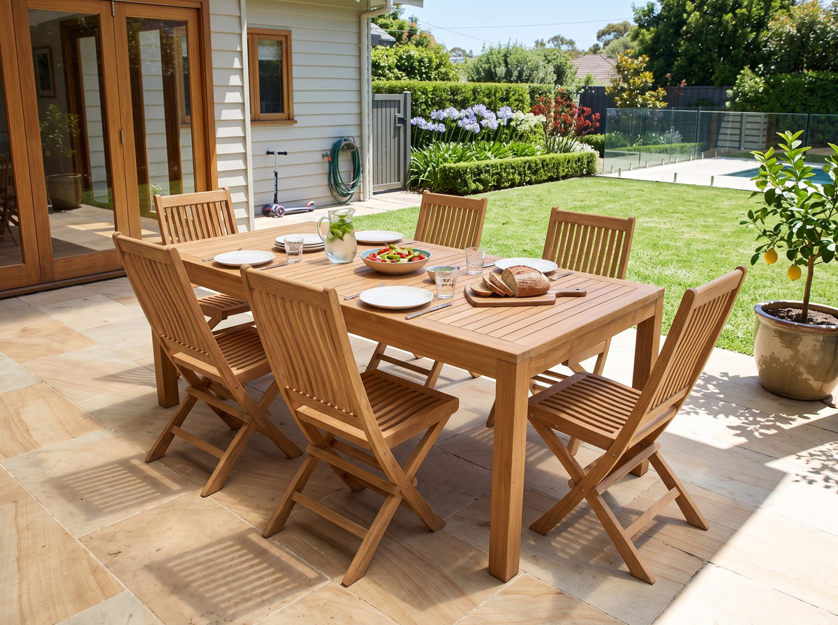 Teak Leo folding dining chairs around a teak Deluxe dining table on a sandstone terrace