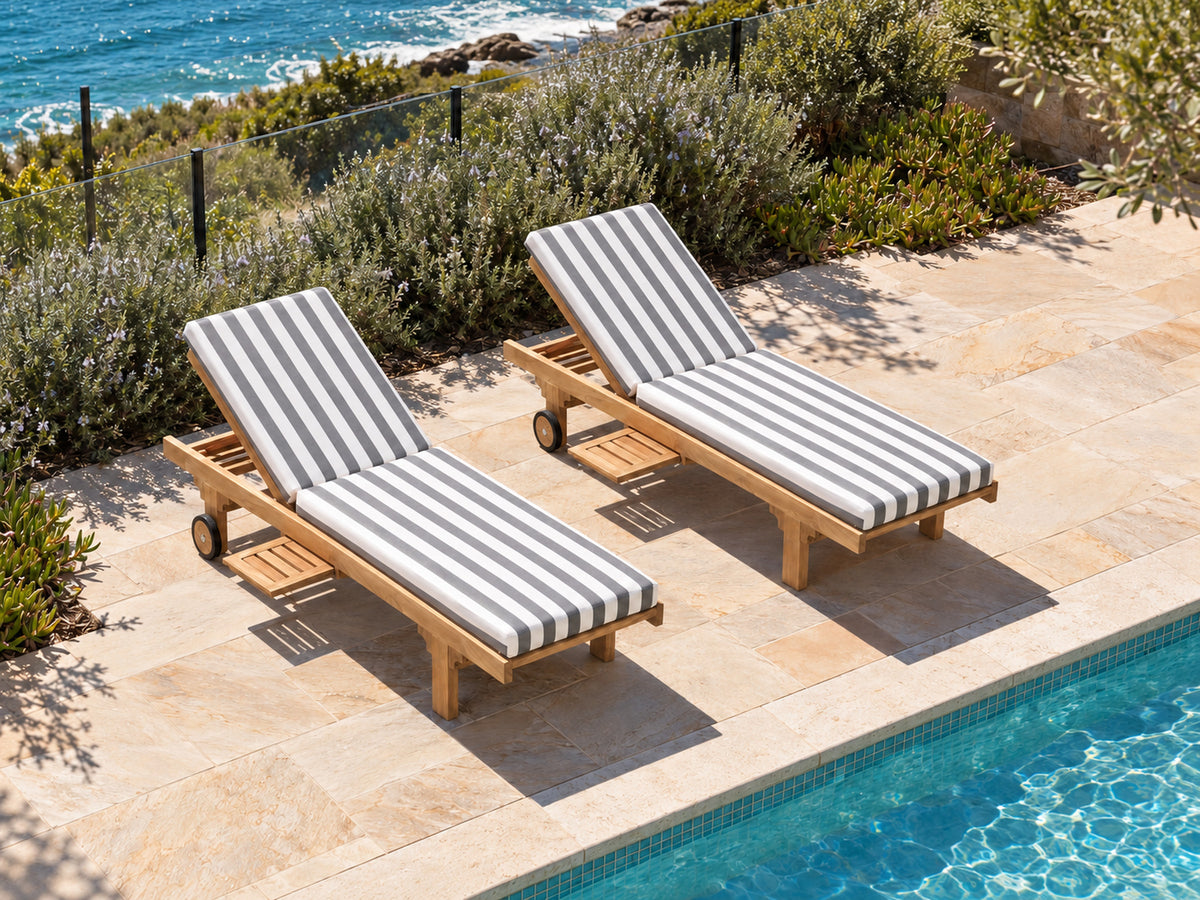 Two Traditional teak pool lounges with denim stripe cushions on sandstone paving in a coastal garden