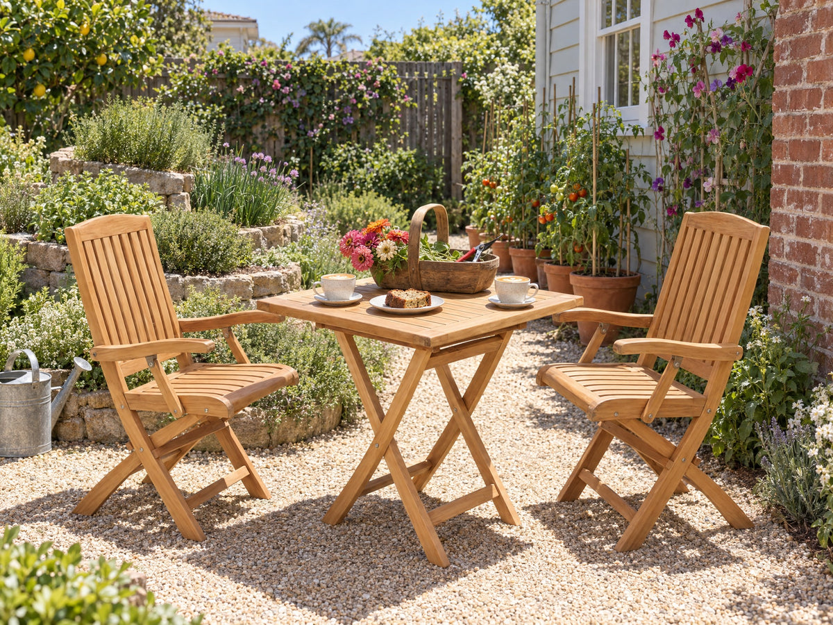 Two teak Vivienne folding armchairs at a square teak folding table on a sunny gravel courtyard